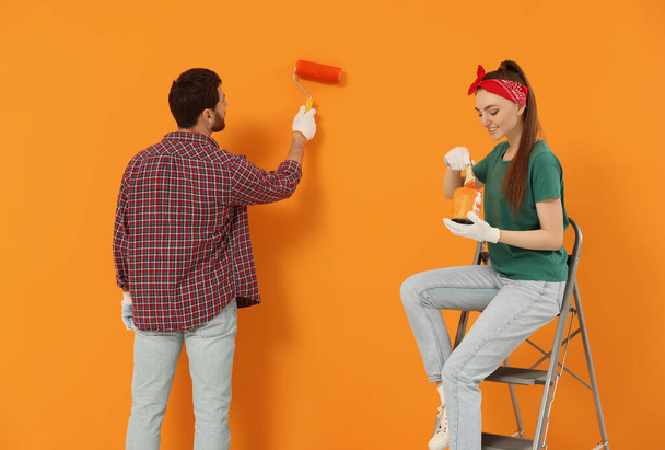 男はブラシで染料の缶を保持オレンジ壁と幸せな女性を描く。インテリアデザイン - 写真・画像