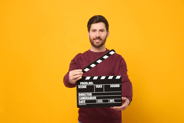 Smiling actor holding clapperboard on orange background, space for text - Valokuva, kuva