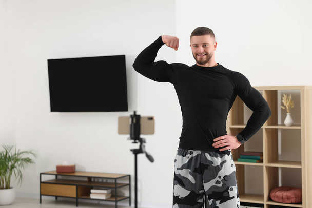 Trainer showing his muscles while streaming online fitness lesson with phone at home - Foto, Bild