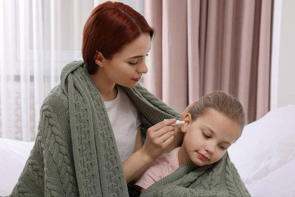 Mother dripping medication into daughter's ear while being wrapped in warm plaid at home - Φωτογραφία, εικόνα