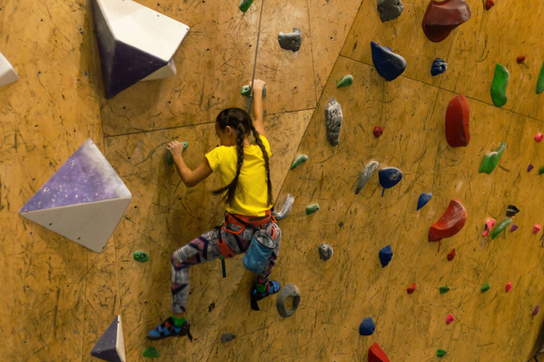 bouldering, little girl climbing up the wall and climber multicolored grips. Leisure activity. - Φωτογραφία, εικόνα
