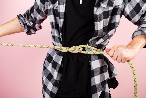 A young traveller or a rock climber with a rope attached to his belt is climbing upwards. copy space, mockup. isolated on pink background. - Foto, Imagen
