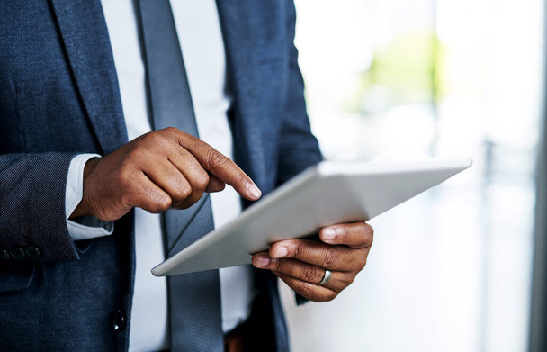 La forma correcta de hacer negocios es mantenerse conectado. un hombre de negocios irreconocible usando una tableta digital mientras está de pie en una oficina moderna - Foto, imagen