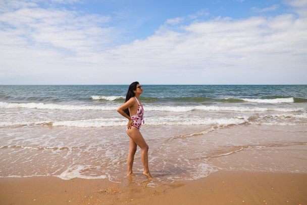 Beautiful and young latin woman is walking along the shore of the beach and posing for photos. Beautiful woman is on holiday on a paradise beach. Holiday and travel concept. - Photo, image