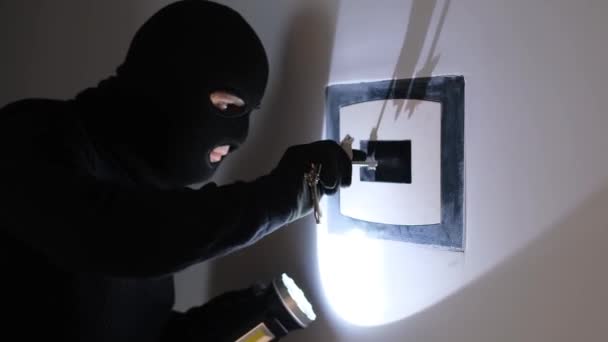 Um ladrão de homens com uma máscara preta e com uma lanterna abre a porta de um cofre em uma casa, apartamento. Falta de alarme e segurança da casa. - Filmagem, Vídeo