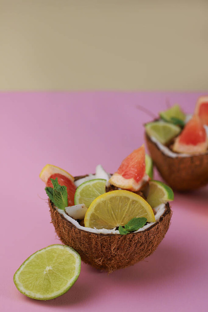 healthy hearty breakfast of coconut flakes, chocolate flakes with slices of citrus lime lemon and grapefruit in a coconut shell on a pink background - Фото, зображення