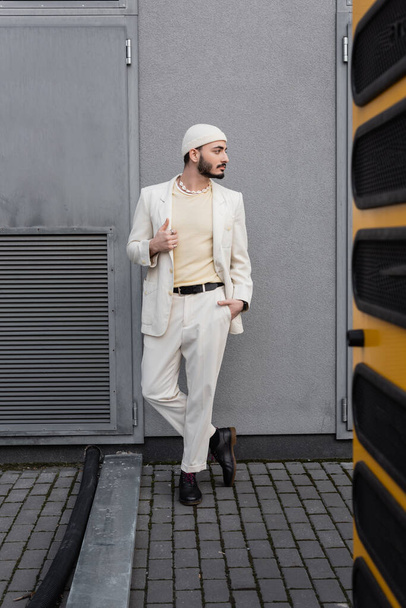 Stylish gay man in hat and suit posing near building on urban street  - Фото, зображення