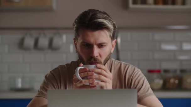 Un homme avec une tasse de café dans les mains regarde des vidéos drôles sur un ordinateur portable. Un homme indépendant travaillant à distance sur un ordinateur a pris une courte pause café. Images 4k de haute qualité - Séquence, vidéo