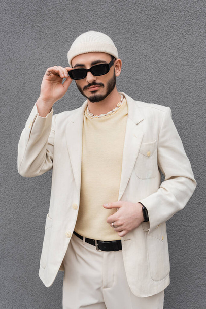 Trendi homoszexuális férfi bézs öltönyben megérinti napszemüveg szabadban  - Fotó, kép