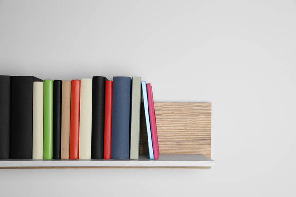 Different books on wooden shelf near white wall, space for text - Foto, Imagen