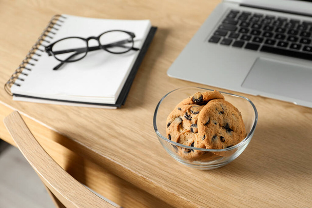 Chocolate chip cookies, notebook and laptop on wooden table at workplace - Foto, imagen