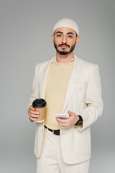 Stylish homosexual man in suit holding smartphone and coffee to go isolated on grey   - Foto, immagini