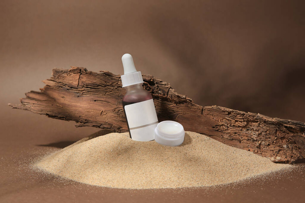 Cosmetic products and tree bark on sand against brown background - Foto, immagini