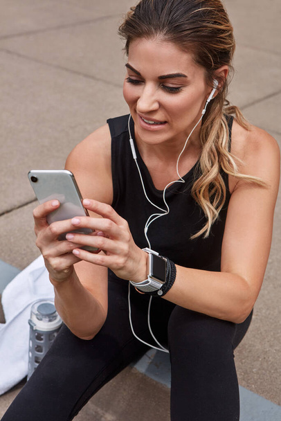Its easier to monitor my progress with some fitness apps. a sporty young woman using a cellphone while exercising outdoors - Photo, Image