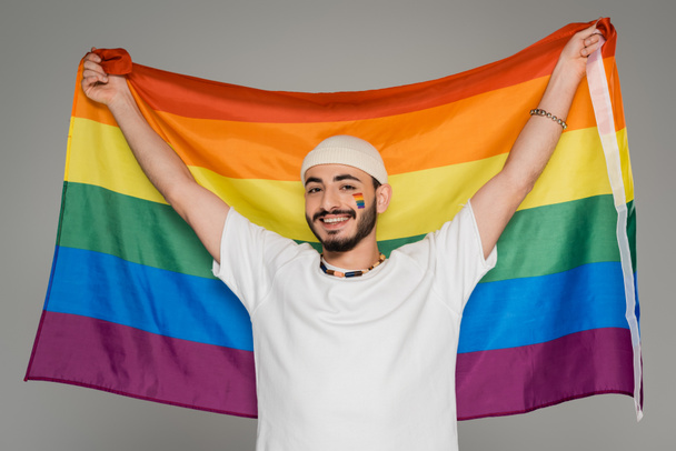 uśmiechnięty homoseksualista w kapeluszu trzymając flagę lgbt odizolowany na szary   - Zdjęcie, obraz