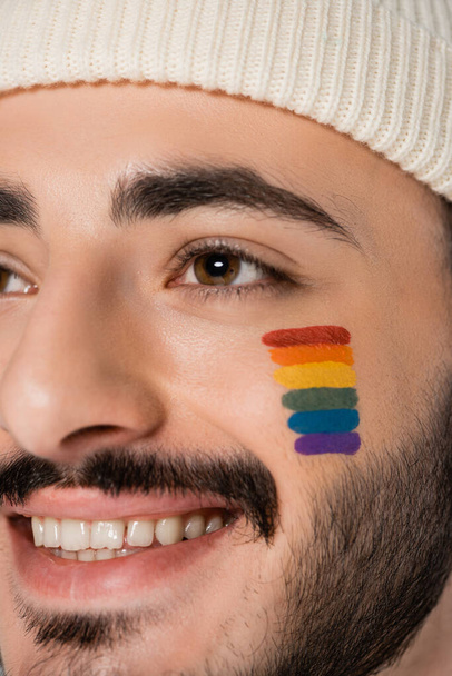 Ausgeschnittene Ansicht eines lächelnden homosexuellen Mannes mit lgbt-Fahne auf der Wange, der wegschaut  - Foto, Bild
