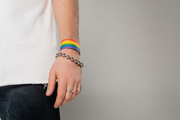 Vista recortada del hombre homosexual con lgbt pulsera en la mano de pie aislado en gris   - Foto, imagen