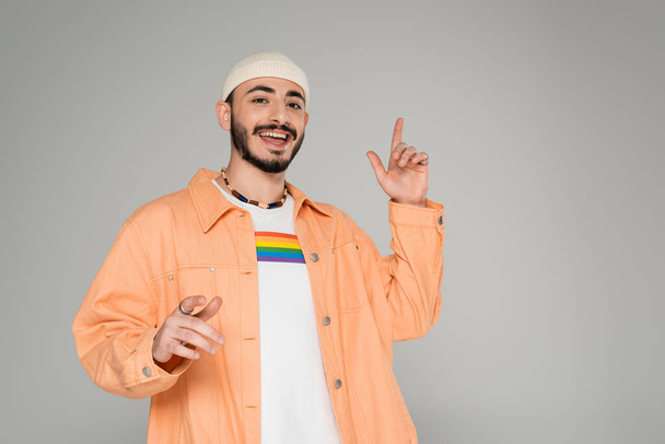 Stylish gay man with lgbt flag on t-shirt pointing with fingers isolated on grey   - Foto, afbeelding