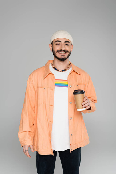 Smiling homosexual man with lgbt flag on t-shirt holding coffee to go isolated on grey   - Photo, Image
