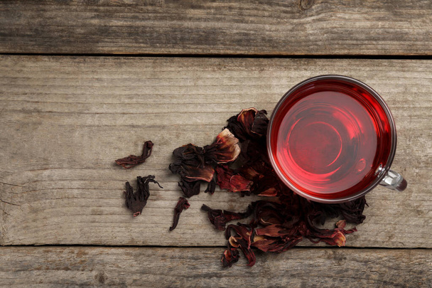 Cup of fresh hibiscus tea and dry flower leaves on wooden table, flat lay. Space for text - Fotoğraf, Görsel