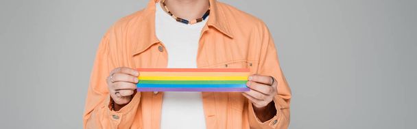 Обрезанный вид стильного гея, держащего флаг lgbt изолированный на сером, баннер  - Фото, изображение