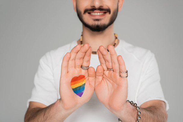 Ausgeschnittene Ansicht eines fröhlichen homosexuellen Mannes mit lgbt-Fahne an der Hand isoliert auf grau, Internationaler Tag gegen Homophobie - Foto, Bild