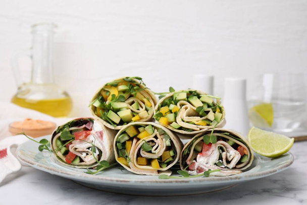 Delicious sandwich wraps with fresh vegetables and slice of lime on white marble table - Photo, image