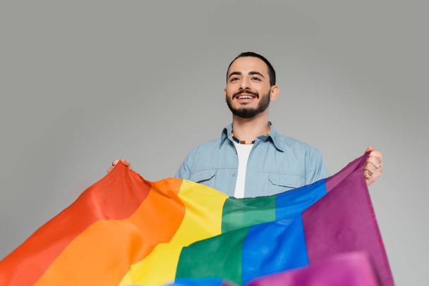 陽気な若いゲイの男は、グレーに隔離されたlgbtフラグを保持します,同性愛嫌悪に対する国際デー - 写真・画像