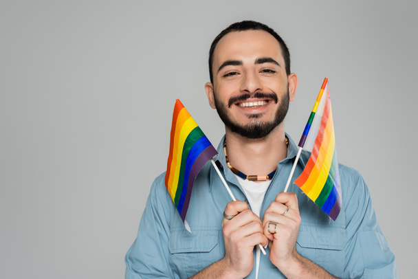 Gelukkig homoseksuele man met lgbt vlaggen en kijken naar camera geïsoleerd op grijs   - Foto, afbeelding