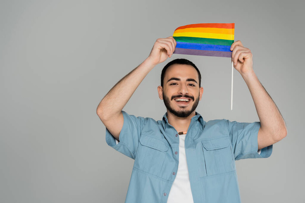 Positive homosexual man holding lgbt flag isolated on grey with copy space, International Day Against Homophobia  - Photo, Image