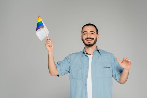 brodaty gej człowiek w koszula uśmiech i gospodarstwa tęcza lgbt flaga izolowane na szary   - Zdjęcie, obraz