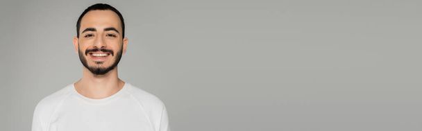 Young bearded gay man in white t-shirt looking at camera isolated on grey, banner   - Foto, Imagem