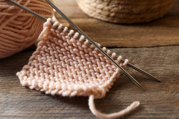 Soft beige knitting and metal needles on wooden table, closeup - Φωτογραφία, εικόνα