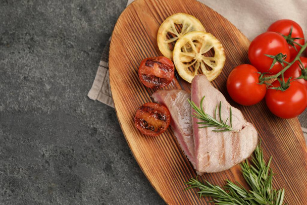 Pieces of delicious tuna steak with rosemary, tomatoes and lemon on grey table, top view. Space for text - Φωτογραφία, εικόνα