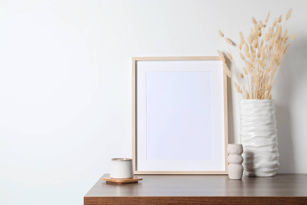 Empty photo frame, cup and vase with dry decorative spikes on wooden table. Mockup for design - 写真・画像