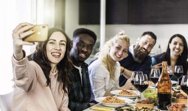 Tipos multiétnicos y mujeres tomando selfie para el almuerzo en la cocina casera - Jóvenes amigos divirtiéndose juntos en el apartamento mientras comen deliciosos espaguetis italianos con salsa de tomate - Filtro brillante - Foto, Imagen