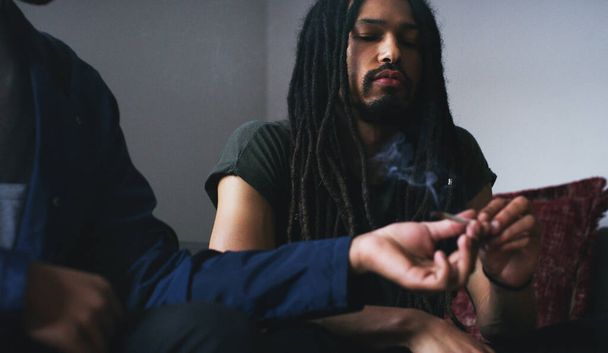 Puff, puff, pass. two young men smoking a marijuana joint at home - Foto, afbeelding