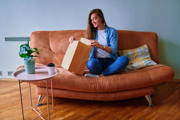 Smiling satisfied happy casual adult joyful young millennial girl customer received cardboard bags with takeaway food and drinks at home. Fast delivery service concept - Foto, Imagem
