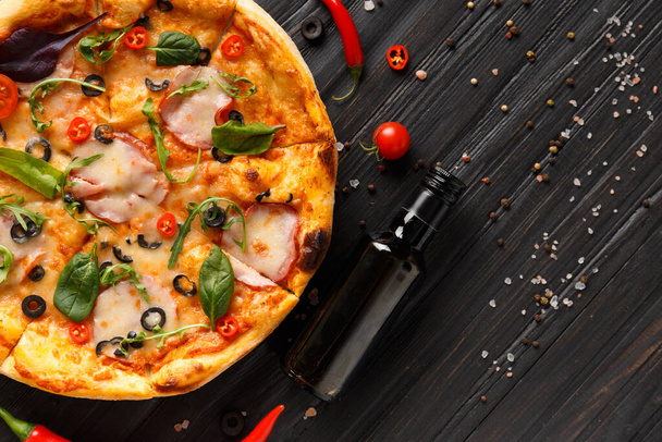 Πίτσα με καπνιστό, ελιές, τυρί και μυρωδικά σε σκούρο ξύλινο φόντο, πάνω όψη. Σπιτική πίτσα με κρέας, σάλτσα και φρέσκα λαχανικά. Παραδοσιακό ιταλικό φαγητό. - Φωτογραφία, εικόνα