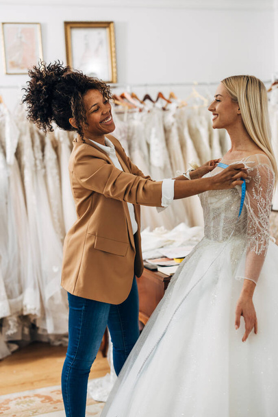 A beautiful happy bride is in a bridal tailoring salon with a tailor - Foto, immagini