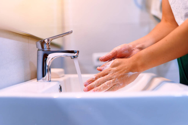Female washing her hands using liquid disinfectant soap and running water in bathroom close up. Personal hand hygiene, health care - Foto, afbeelding