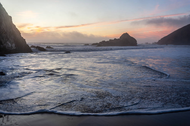 プファイファービーチには波が流れていますが、紫色の夕日に包まれています。. - 写真・画像