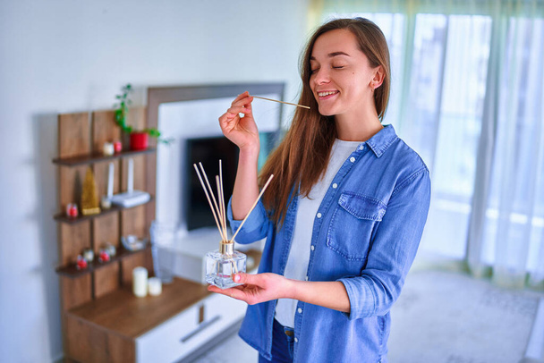 Junge glücklich lächelnde niedliche Frau genießt Aroma und Geruch von Schilfrohr Lufterfrischer im Wohnzimmer zu Hause  - Foto, Bild