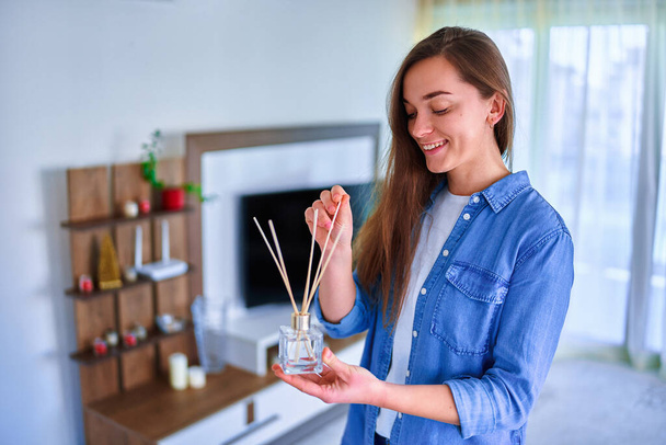 Woman enjoying aroma and smell of reed air freshener in the living room at home  - Photo, Image