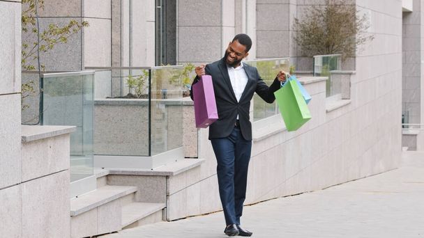 Male ethnic customer client buyer man holding shopping bags buying in fashionable store trendy mall clothes shop. Businessman African American male in city with purchases enjoy Black Friday discounts - Photo, Image
