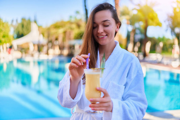 Young happy smiling woman enjoy of relaxing summer vacations with refreshing Pina colada cocktail by the pool at the all-inclusive resort  - Фото, зображення