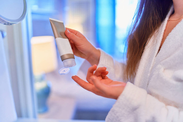 Female applies a nourishing cream to moisturize her hands after shower. Hand care  - Fotografie, Obrázek