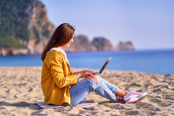 Young happy joyful carefree satisfied millennial freelancer girl using laptop on beach by the sea. Dream office work concept - Zdjęcie, obraz