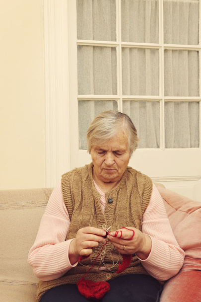 Donna anziana che lavora a maglia con lana rossa
 - Foto, immagini