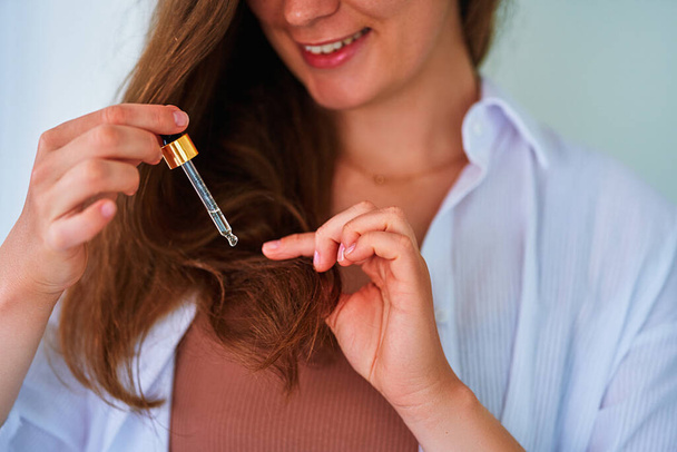 Brunette woman using dropper for pampering and moisturizing hair ends with vitamin essential oil serum - Foto, afbeelding